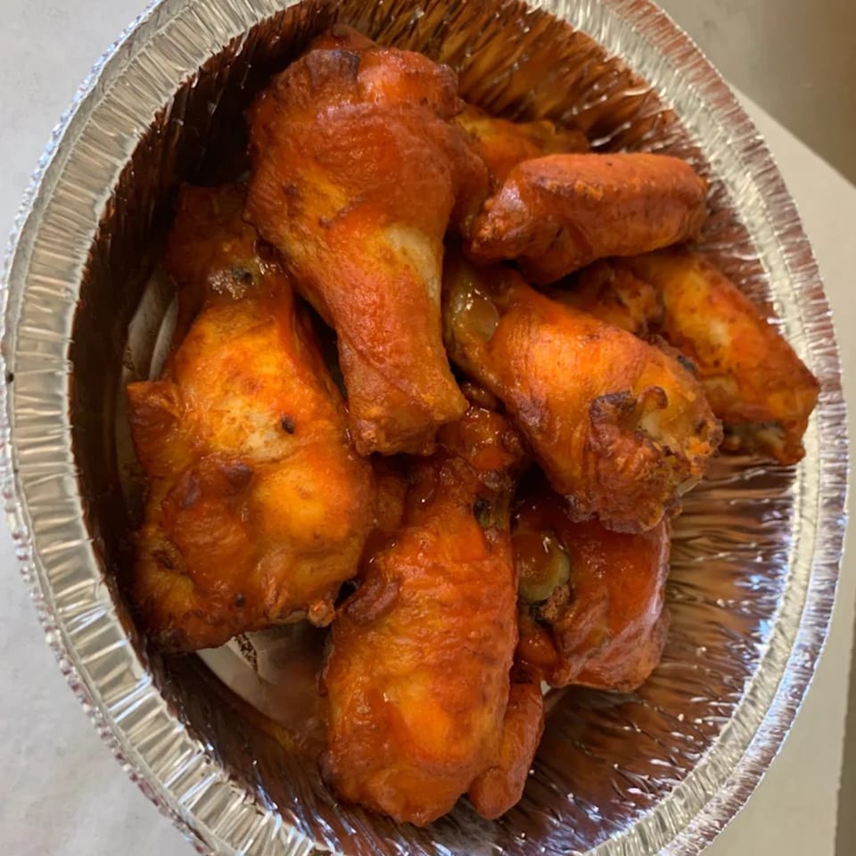 A close-up of several buffalo chicken wings in a foil container from 7th Street Pizza.