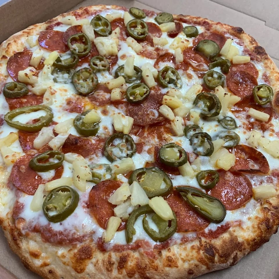 A 7th Street Pizza pepperoni pizza with pineapple and jalapeños in a cardboard box.