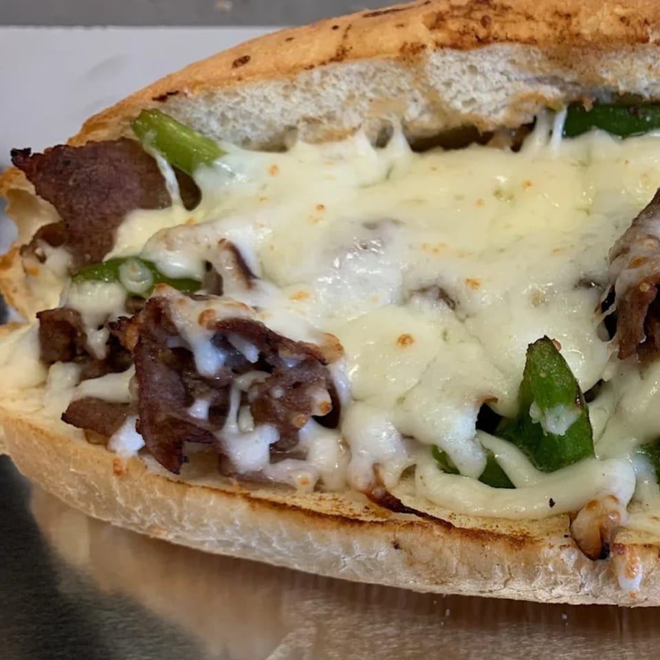Close-up of a cheesesteak sandwich from 7th Street Pizza, with melted cheese, steak, and green peppers.