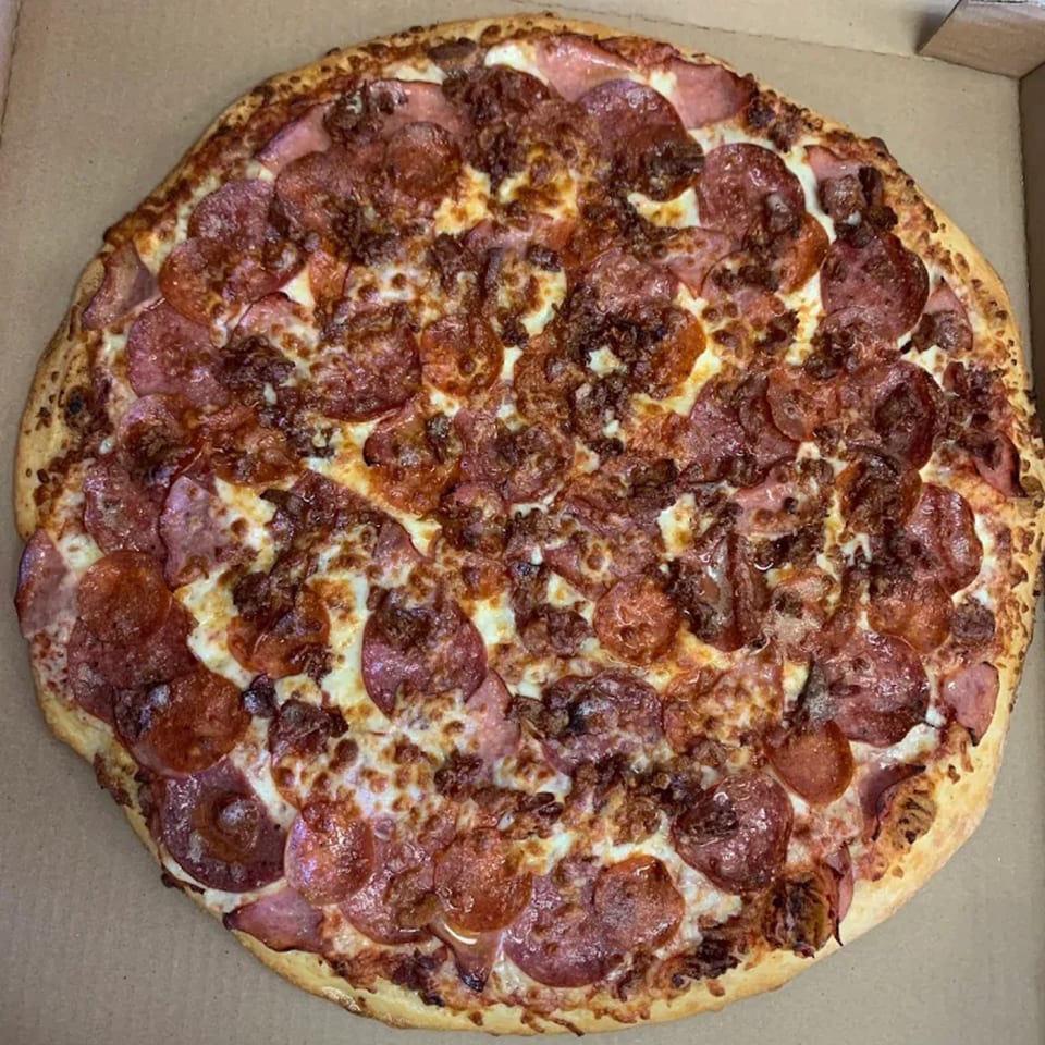 A large, round 7th Street Pizza with pepperoni, ham, and sausage in a cardboard box.