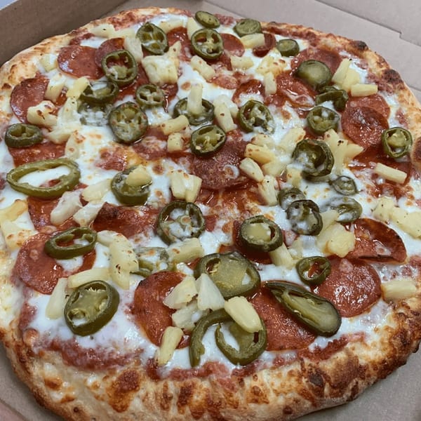 A 7th Street Pizza pepperoni pizza with pineapple and jalapeños in a cardboard box.