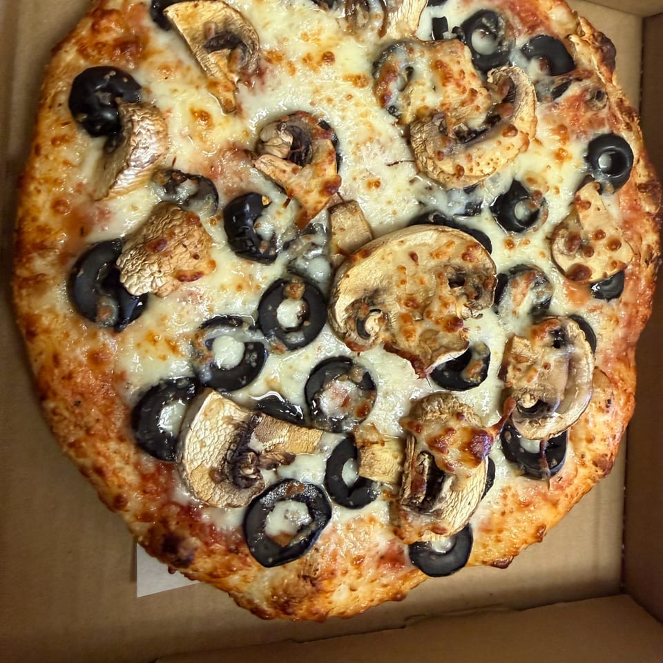Whole pizza with melted cheese, sliced mushrooms, and black olives in a delivery box.