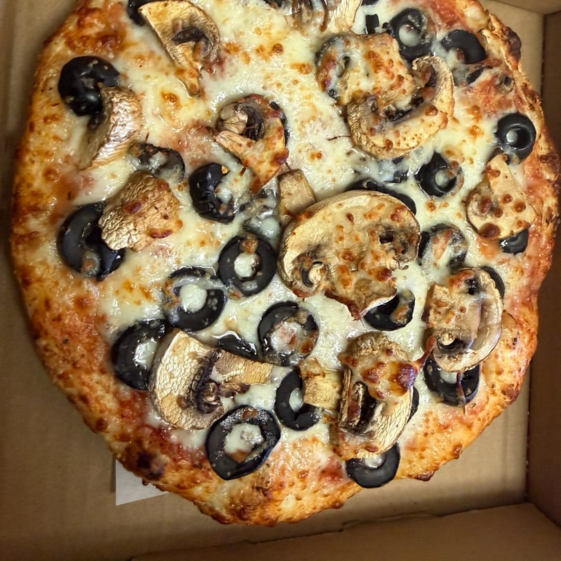 Whole pizza with melted cheese, sliced mushrooms, and black olives in a delivery box.