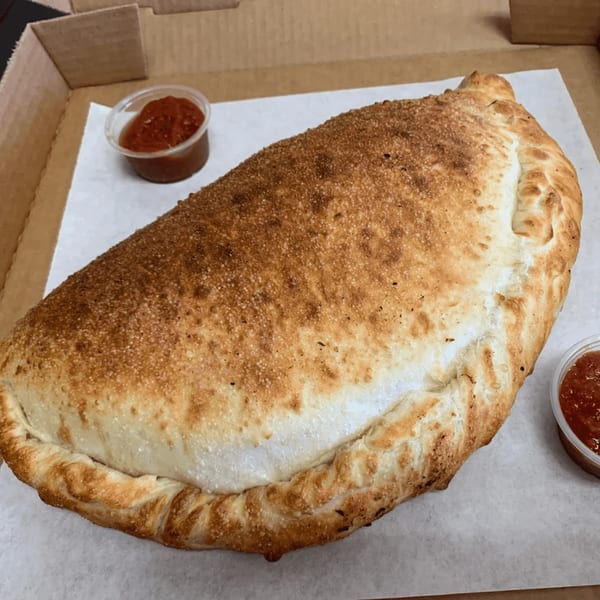 A large, golden-brown calzone with two small cups of marinara sauce in a pizza box.
